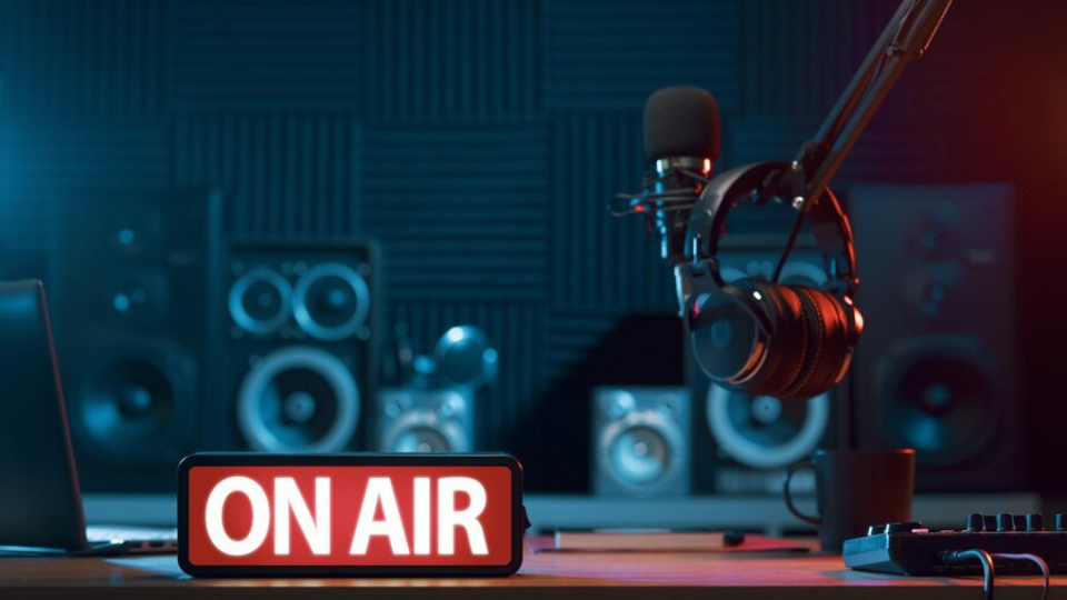 An image showing a modern radio studio with headphones, a microphone, and an illuminated 'ON AIR' sign.